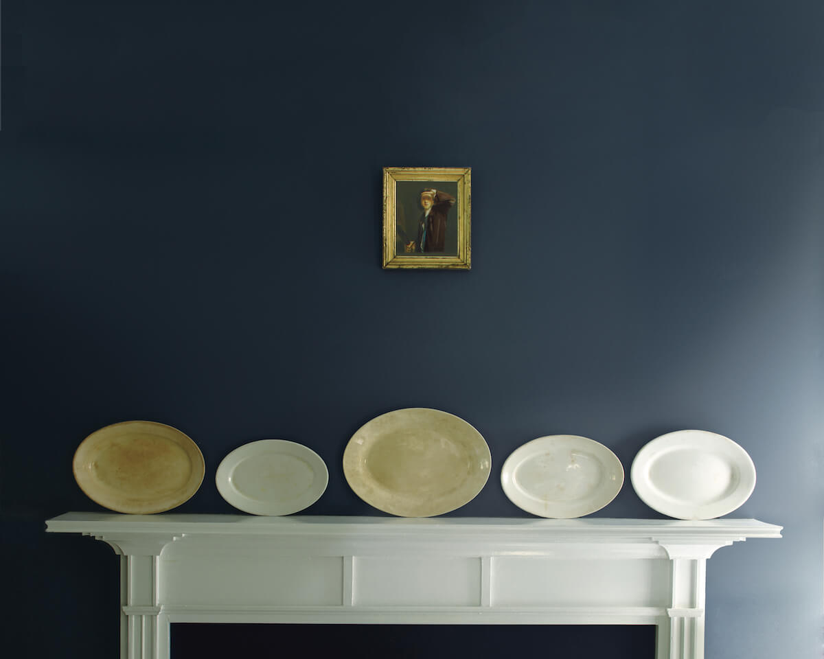 Deep blue accent wall with decorative plates against white mantle.